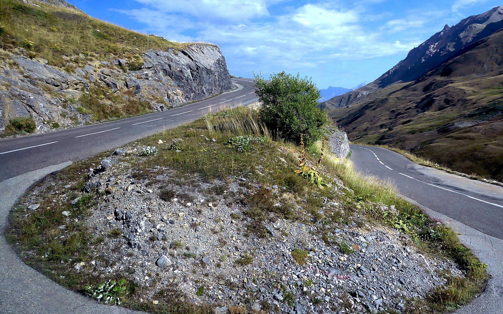 The Col du Galibier road hairpins seen from above, grey asphalt cutting across bare scree in high-altitude light