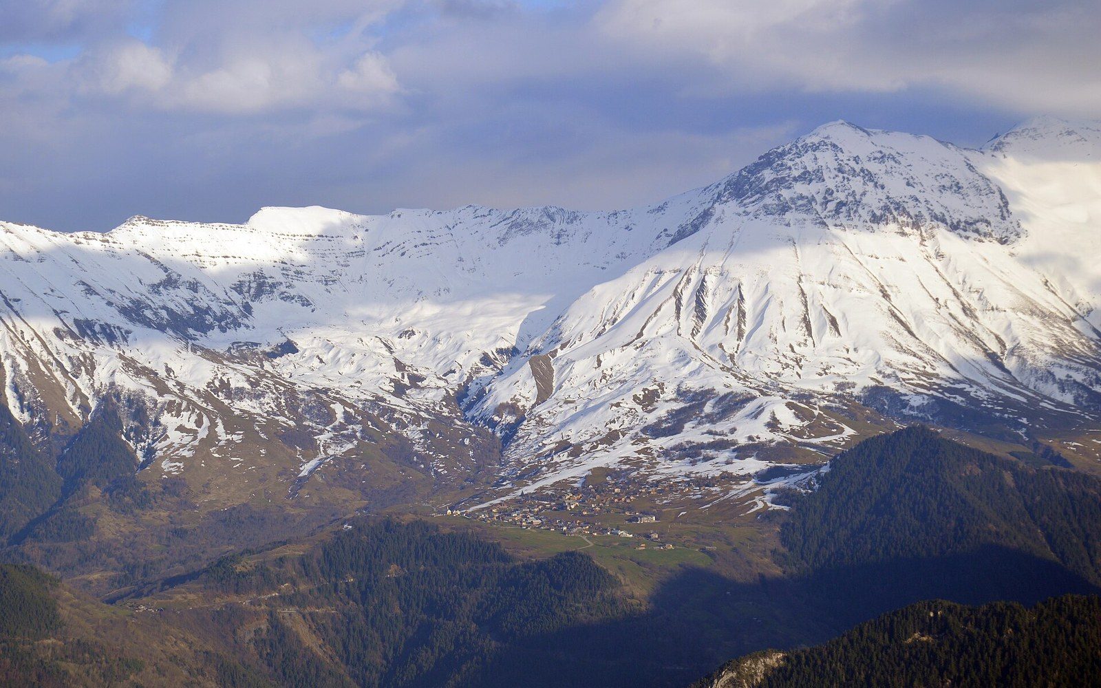Snow-streaked mountain ridges tower over a small alpine village nestled in the valley below