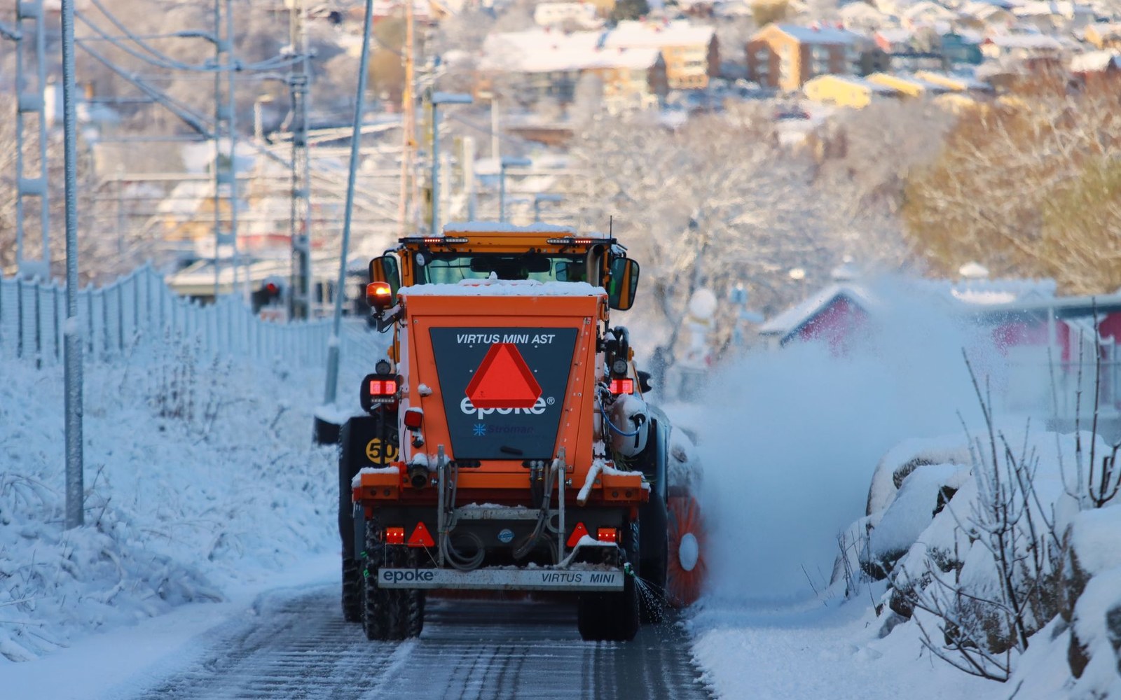 A rotary snow-clearance machine cutting through a deep snow wall on a high col road in June, two operators visible in the cab